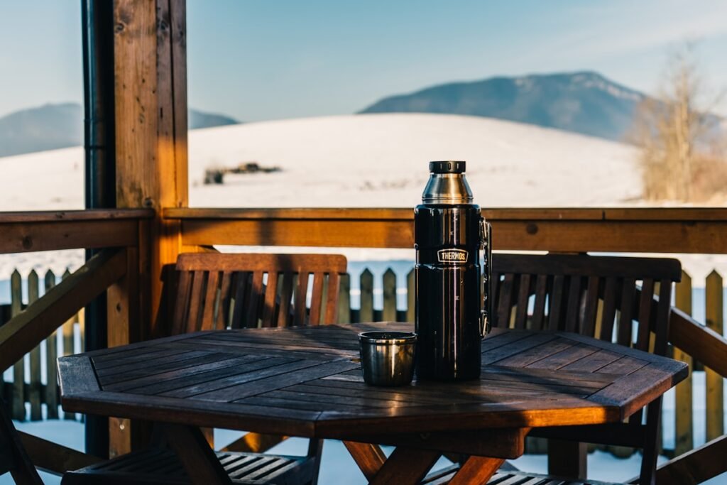 Thermosfles op een houten tafel op een besneeuwd terras, urenlang warm gehouden